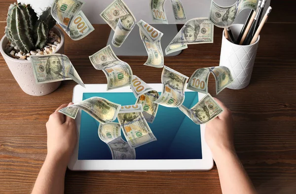 Человек с современным планшетом и летающими долларовыми банкнотами за столом, крупным планом. Люди зарабатывают деньги в интернете — стоковое фото