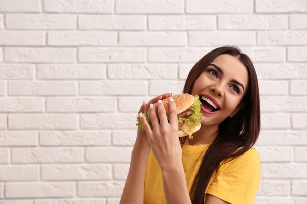 レンガの壁の近くのおいしいハンバーガーを食べる若い女性。テキストのためのスペース — ストック写真