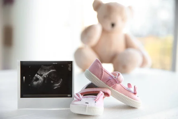 Foto de ultra-som do bebê e botas bonitos na mesa dentro de casa — Fotografia de Stock