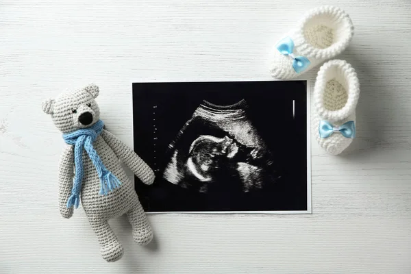 Ultra-som foto de bebê, brinquedo e botas de malha no fundo de madeira, flat lay — Fotografia de Stock