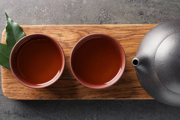 Доска с чашками и чайник свежеваренный улун на сером фоне, вид сверху — стоковое фото