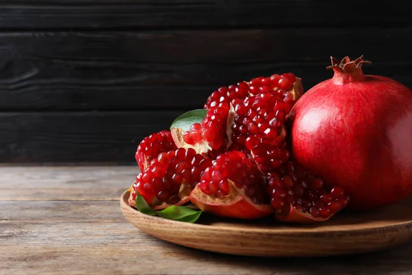 Tallrik med mogna Granatäpplen på träbord mot mörk bakgrund, utrymme för text — Stockfoto