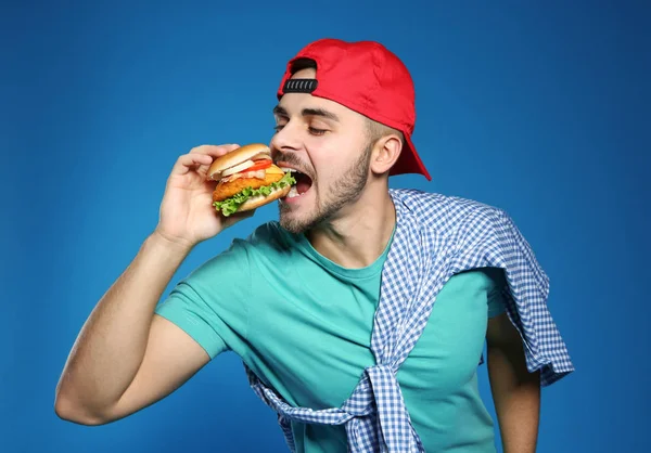 Stilig man äta välsmakande hamburgare på färgbakgrund — Stockfoto