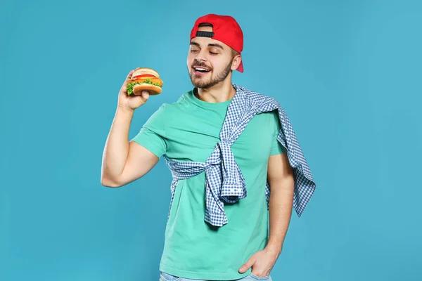 Handsome man with tasty burger on color background — Stock Photo, Image