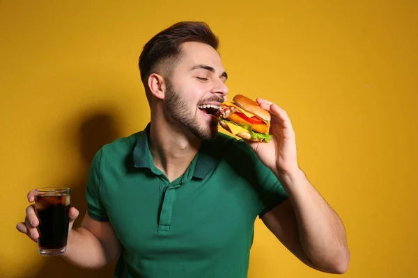 Stilig man med välsmakande hamburgare och cola på färgbakgrund — Stockfoto