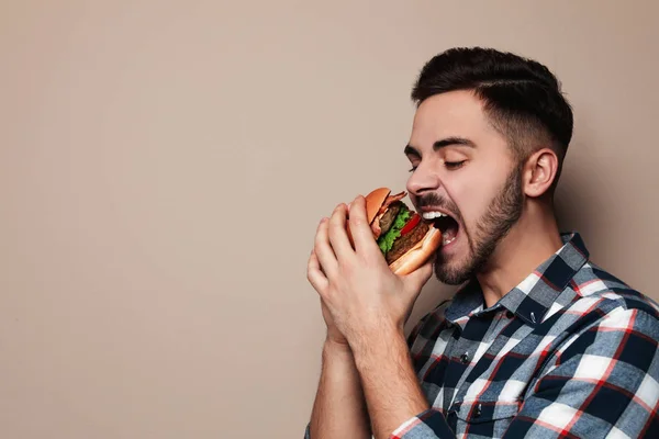 Hombre guapo comiendo sabrosa hamburguesa sobre fondo de color. Espacio para texto —  Fotos de Stock