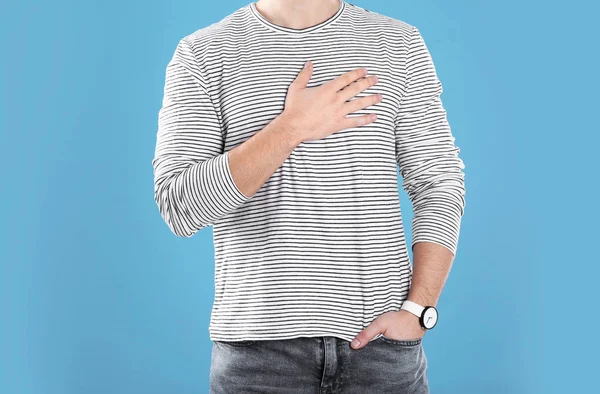 Joven cogido de la mano cerca del corazón sobre fondo de color, primer plano —  Fotos de Stock