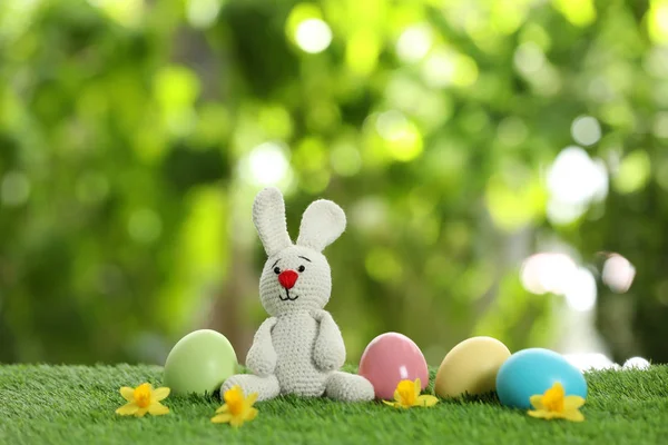 Cute Easter bunny toy and dyed eggs on green grass against blurred background, space for text — Stock Photo, Image