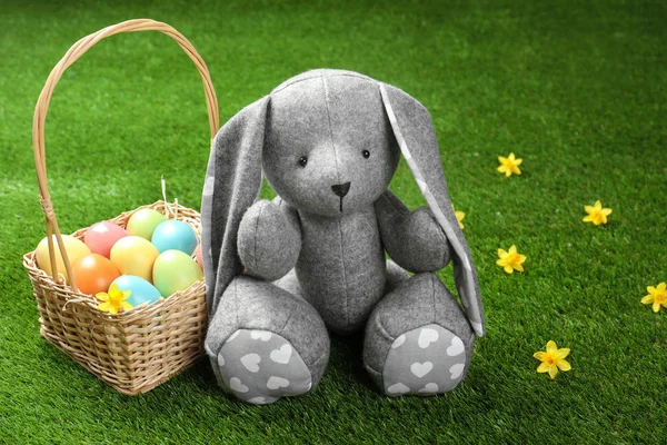 可爱的复活节兔子玩具和柳条篮与绿色草地上染色的鸡蛋, 文本空间 — 图库照片