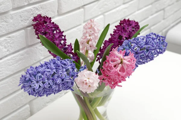 Vackra hyacinter i glasvas på bordet mot tegelvägg. Vårens blommor — Stockfoto