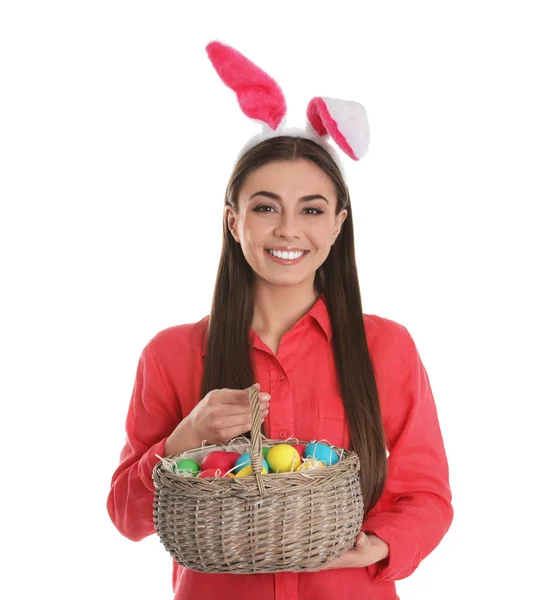 Beautiful woman in bunny ears headband holding basket with Easter eggs on white background — Stock Photo, Image