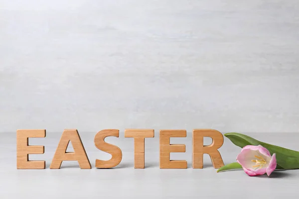 Wort Ostern aus Holzbuchstaben und Frühlingstulpe auf Tisch vor hellem Hintergrund — Stockfoto