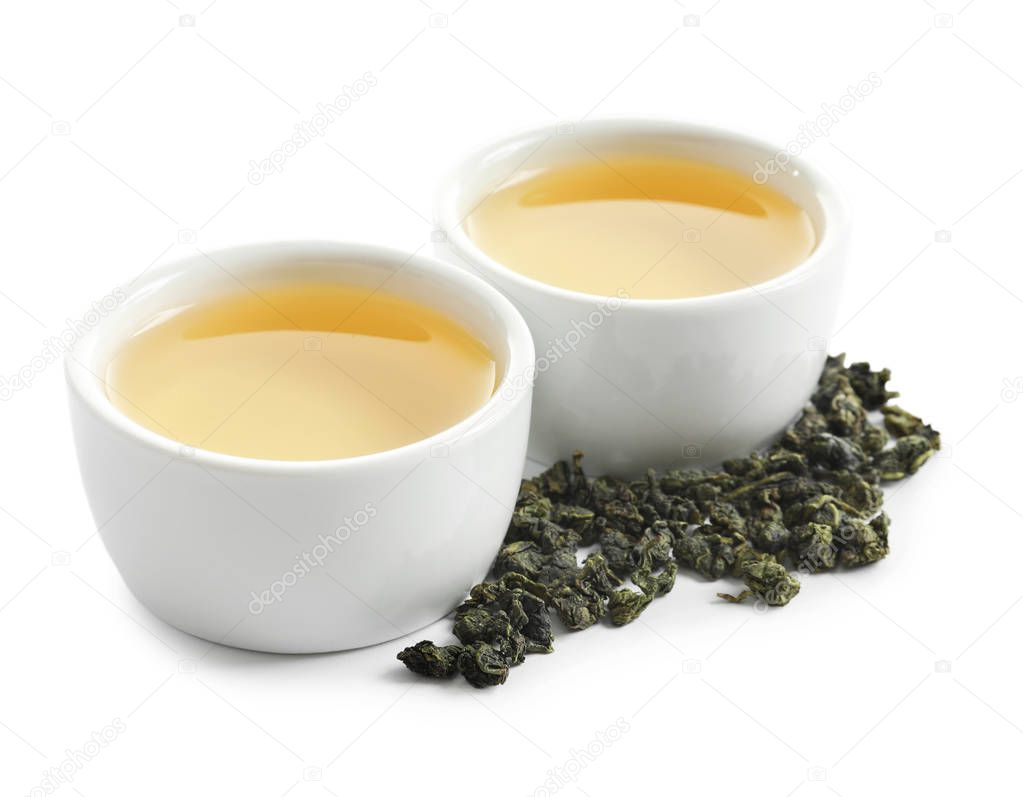 Cups of Tie Guan Yin oolong and tea leaves on white background