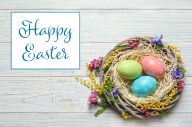 Boyalı yumurta ve çiçeklerle ahşap masa, üstten görünüm üzerinde hasır yuvası. Mutlu Paskalya