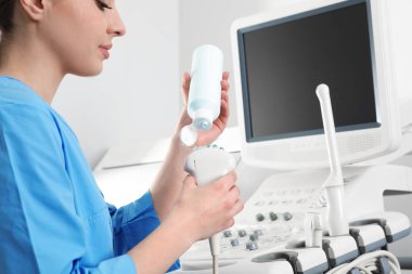 Sonographer covering ultrasound machine probe with gel in clinic, closeup clipart