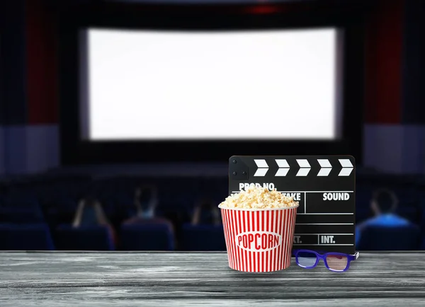 Puchar popcorn, clapperboard i okulary na drewnianym stole w sali kina. Miejsca na tekst — Zdjęcie stockowe