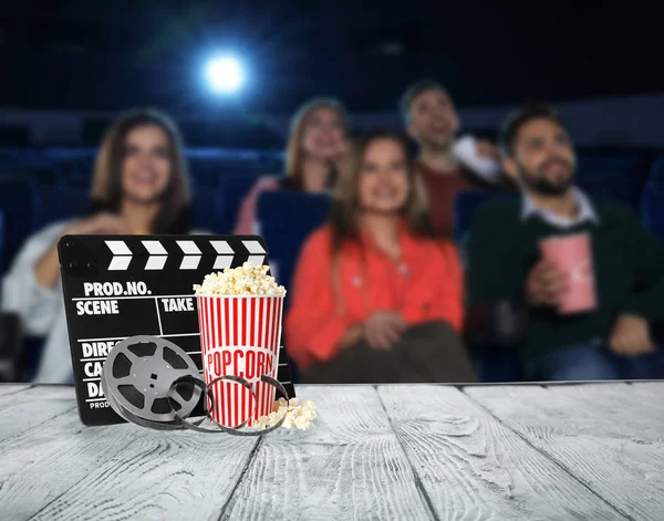 Tasse Popcorn, Klappbrett, Rolle auf Holztisch und Menschen im Kinosaal. Raum für Text — Stockfoto