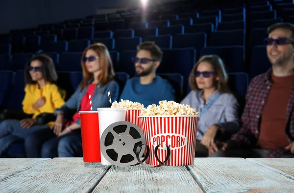 Popcorn, boissons, bobine sur table en bois et les gens dans la salle de cinéma — Photo