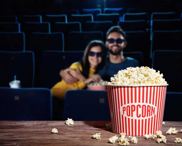 Bucket of popcorn on wooden table in cinema hall. Space for text — Stock Photo, Image