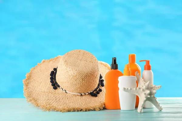 Set con diferentes botellas de crema corporal de protección solar y sombrero sobre mesa de madera contra fondo de color —  Fotos de Stock