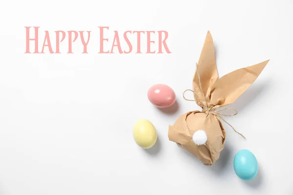 Kreatív nyuszi ajándék táska és festett tojás, fehér háttér, felülnézet. Kellemes húsvéti ünnepeket — Stock Fotó