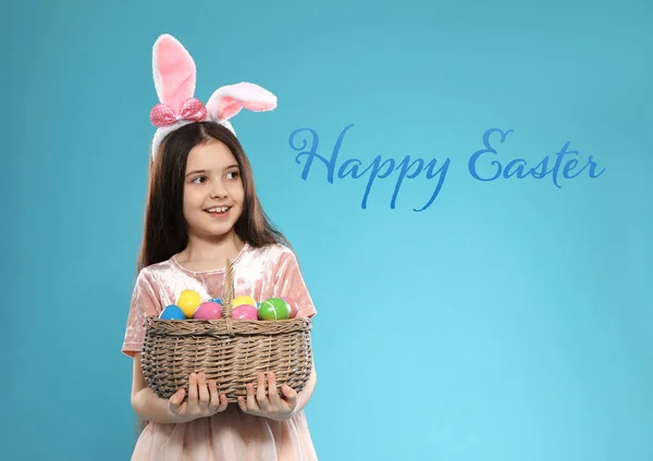 Niña en orejas de conejo diadema celebración cesta con huevos en el fondo de color. Feliz Pascua — Foto de Stock