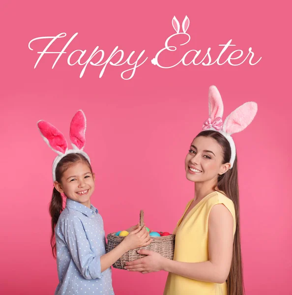 Madre e hija en diademas de orejas de conejo sosteniendo cesta con huevos sobre fondo de color. Feliz Pascua — Foto de Stock