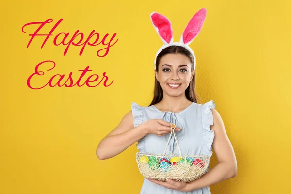Hermosa mujer en orejas de conejo diadema celebración cesta con huevos en el fondo de color. Feliz Pascua — Foto de Stock