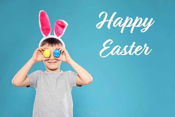 Niño en orejas de conejito diadema sosteniendo huevos cerca de los ojos en el fondo de color. Feliz Pascua — Foto de Stock