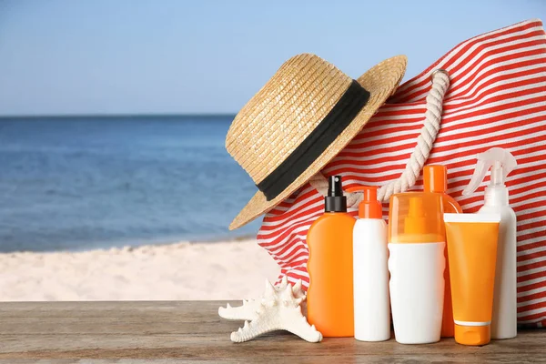 Set avec différentes bouteilles de crème pour le corps de protection solaire et accessoires de plage sur table en bois contre le paysage marin. Espace pour le design — Photo