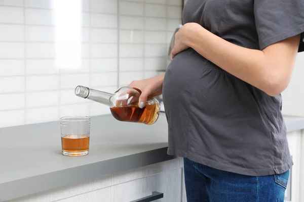 Будущая мать наливает алкоголь из бутылки в стекло на кухне, крупным планом. Плохие привычки во время беременности — стоковое фото