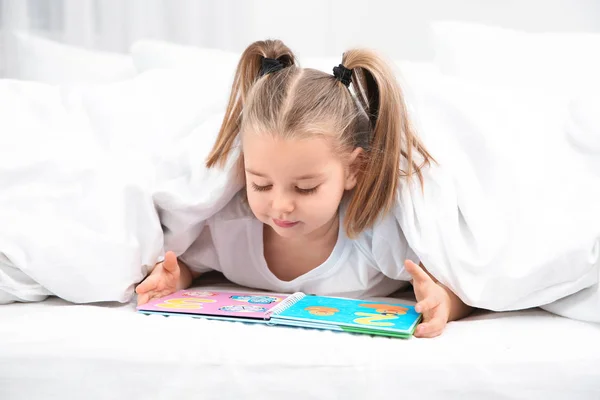 Όμορφο κοριτσάκι με το βιβλίο στο κρεβάτι στο σπίτι. Πρόγραμμα ύπνου — Φωτογραφία Αρχείου