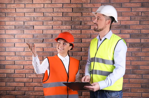 Ingenieros industriales en uniformes con portapapeles sobre fondo de pared de ladrillo. Equipo de seguridad — Foto de Stock