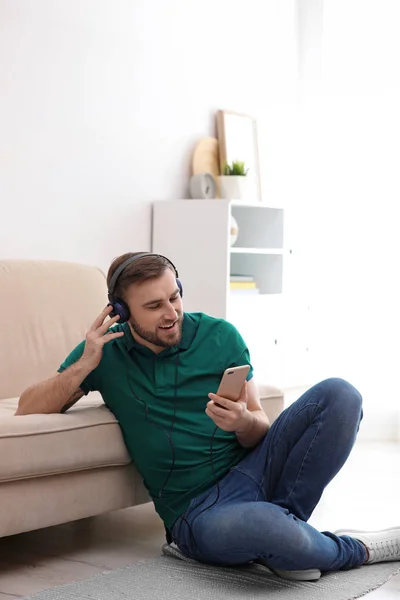 Mladý muž v sluchátka s mobilním zařízením, poslech hudby doma — Stock fotografie