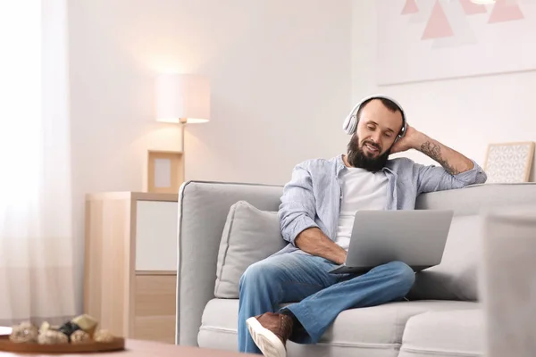 Mature man with headphones and laptop on sofa at home — Stock Photo, Image