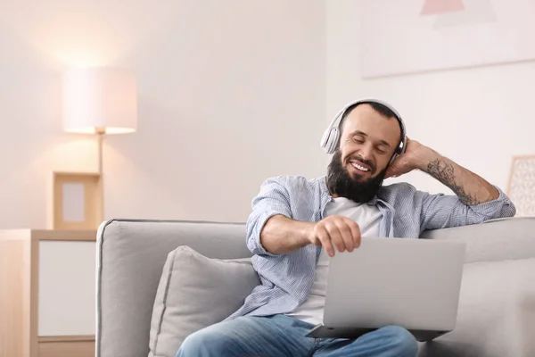 Homem maduro com fones de ouvido e laptop no sofá em casa — Fotografia de Stock