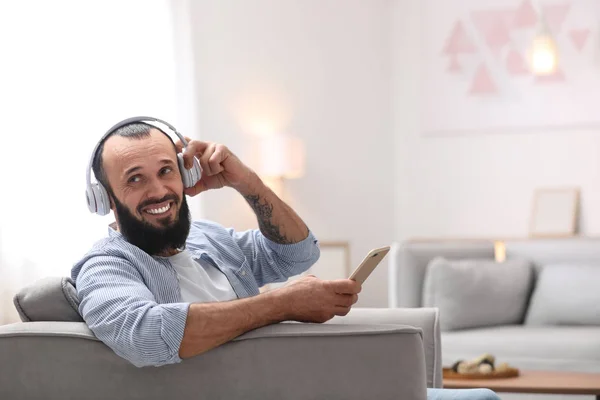 Hombre maduro con auriculares y dispositivo móvil descansando en sillón en casa —  Fotos de Stock