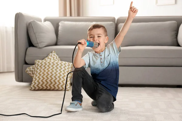 Garoto engraçado bonito com microfone na sala de estar — Fotografia de Stock