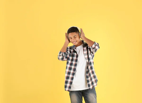 Menino adolescente afro-americano ouvindo música com fones de ouvido no fundo de cor — Fotografia de Stock