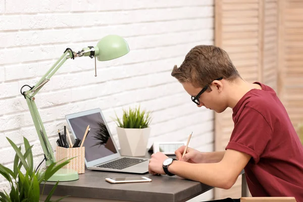 Guapo adolescente haciendo la tarea en la mesa en la habitación —  Fotos de Stock