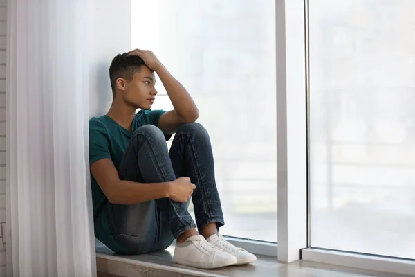 Αναστατωμένος Αφροαμερικανός εφηβικό αγόρι κάθεται μόνος κοντά σε παράθυρο — Φωτογραφία Αρχείου
