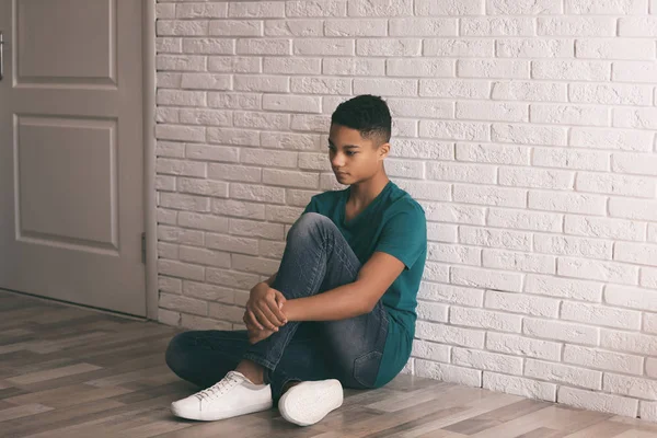 Upprörd afroamerikansk tonårspojke som sitter ensam på golvet nära vägg — Stockfoto