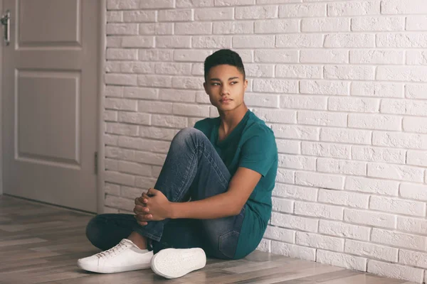 Upset African-American teenage boy sitting alone on floor near wall — Stock Photo, Image