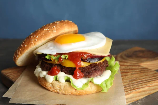 Вкусный бургер с яичницей на борту на цветном фоне — стоковое фото
