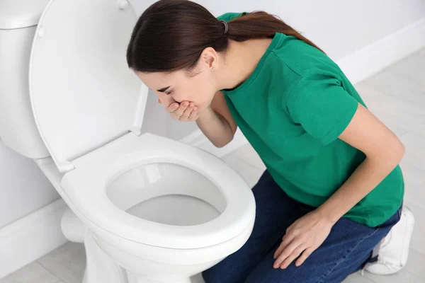 Jonge vrouw die lijdt aan misselijkheid over toilet Bowl binnenshuis — Stockfoto