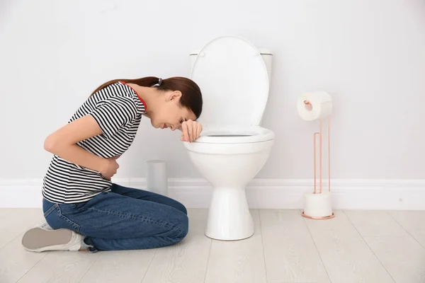 Молода жінка, яка страждає нудотою в туалеті в приміщенні. Простір для тексту — стокове фото
