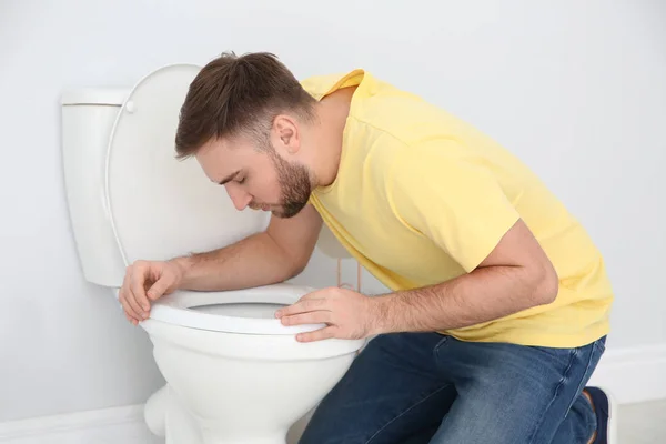 Молодий чоловік страждає від нудоти над туалетом у приміщенні — стокове фото