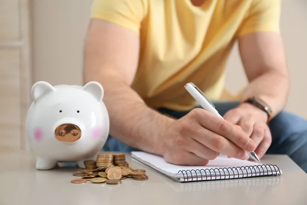 Man met laptop, piggy bank en geld aan tafel binnenshuis, close-up — Stockfoto