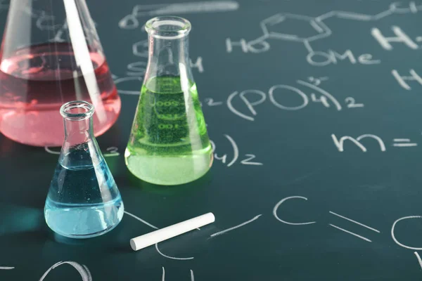 Artículos de vidrio de laboratorio en pizarra con fórmulas químicas, primer plano — Foto de Stock
