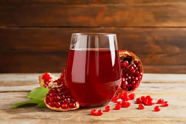 Glas van granaatappelsap en vers fruit op tafel tegen houten achtergrond — Stockfoto